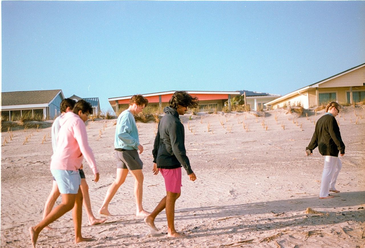 Friends walking barefoot across a sandy beach toward beach houses