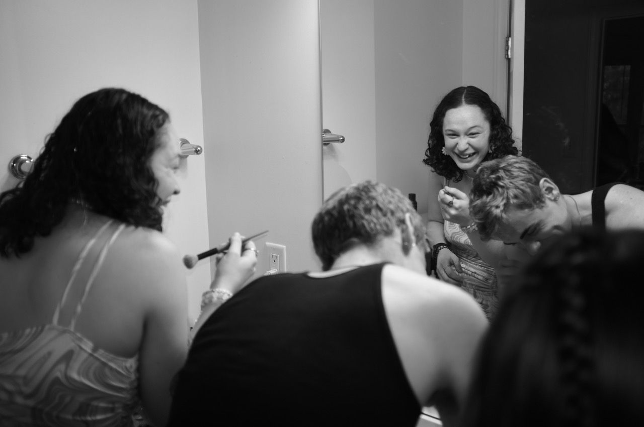 Black and white photo of friends laughing while getting ready in a bathroom mirror