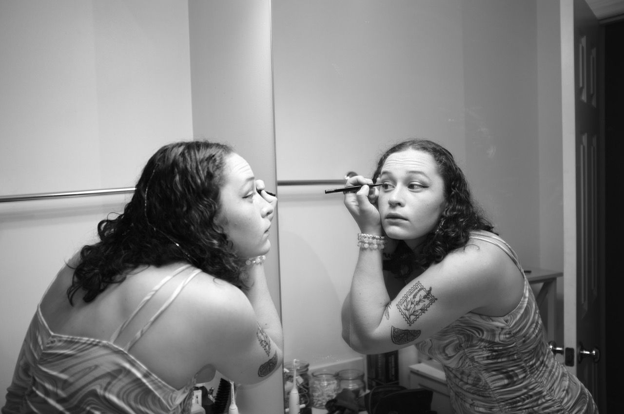 Black and white photo of someone applying eyeliner in a mirror