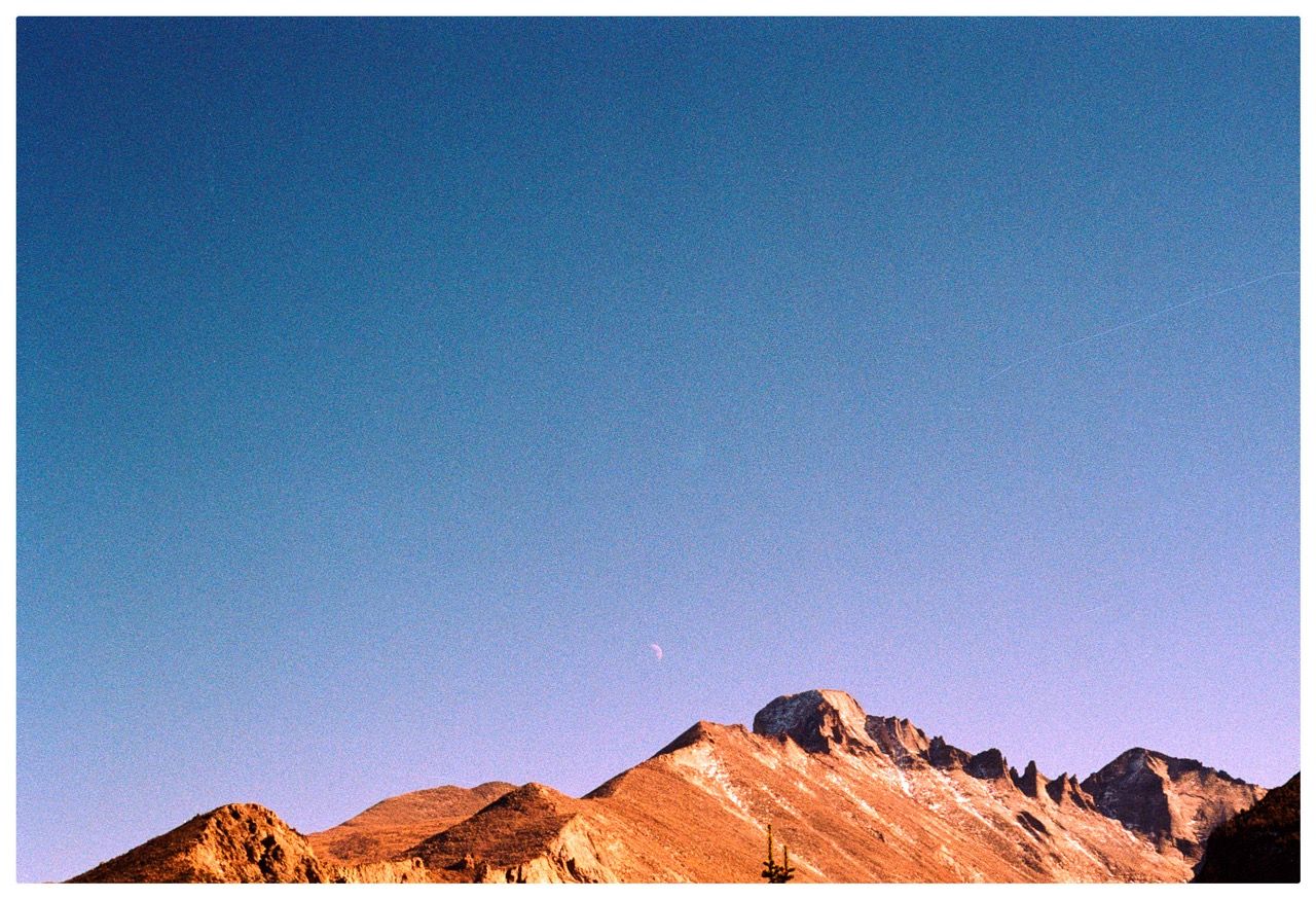 A crescent moon over a jagged mountain ridge at dusk
