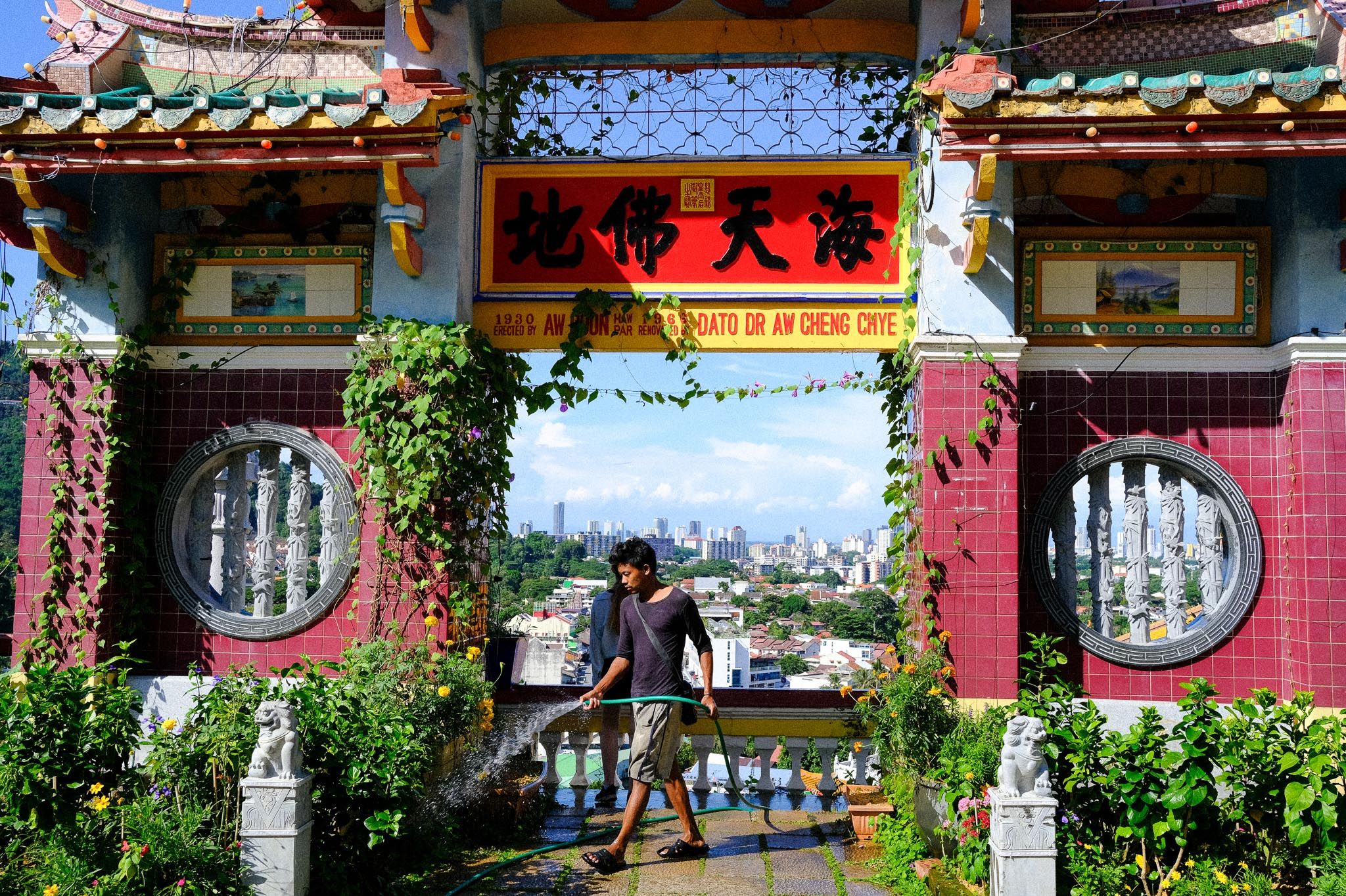A man walking through an ornate temple gate with the city below