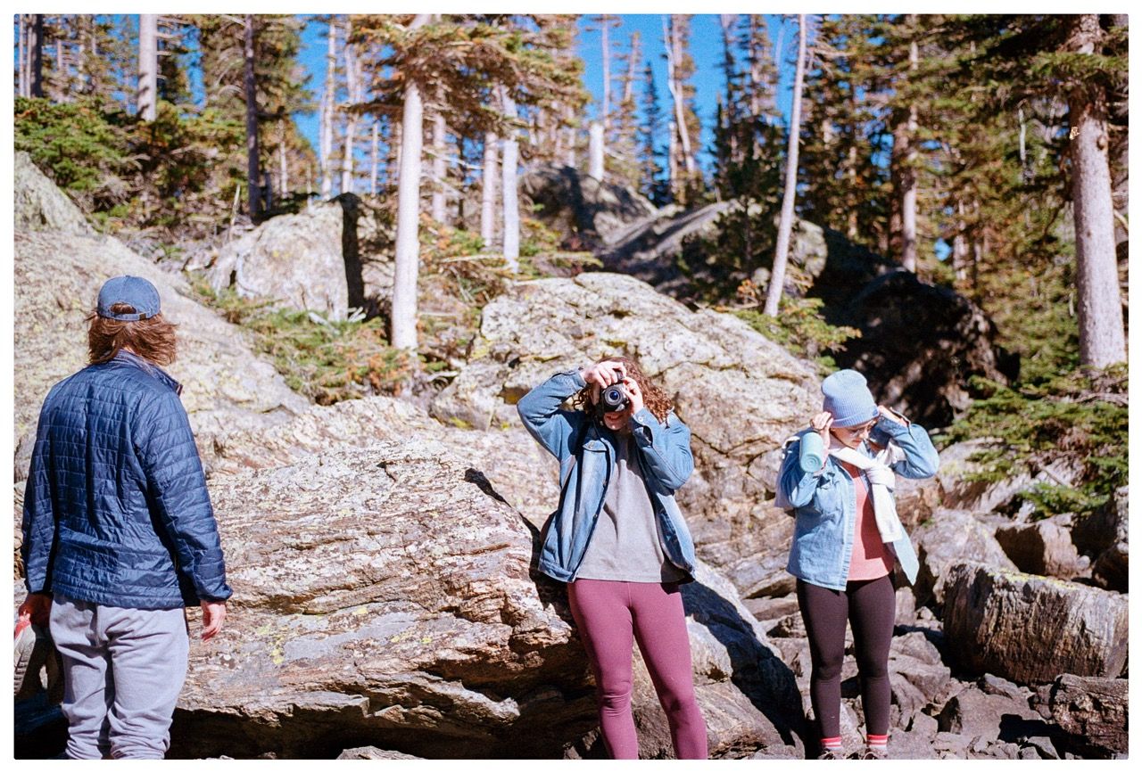 Three hikers among boulders and pines, two of them taking photos