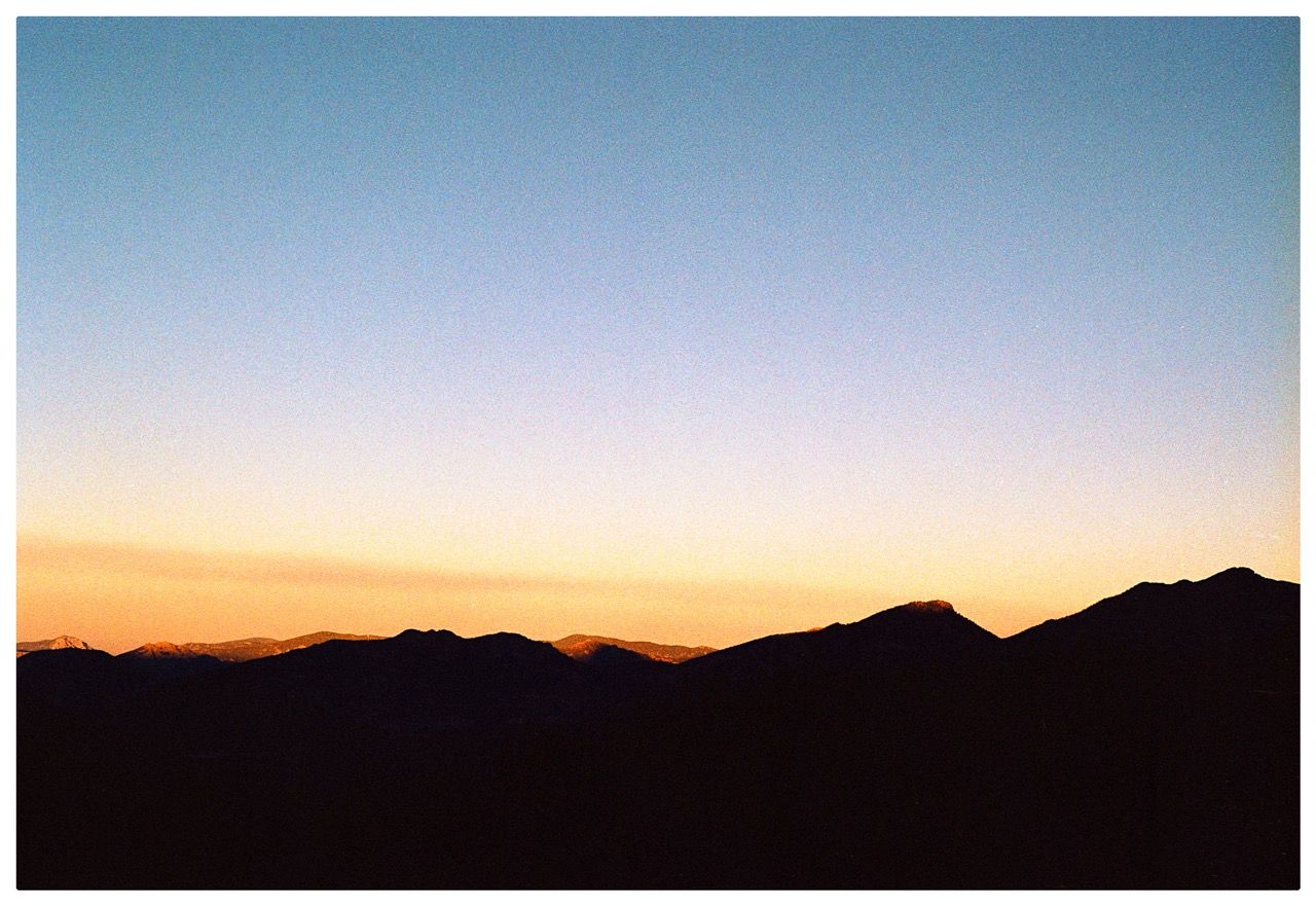 Mountain silhouettes under an orange and blue sky after sunset