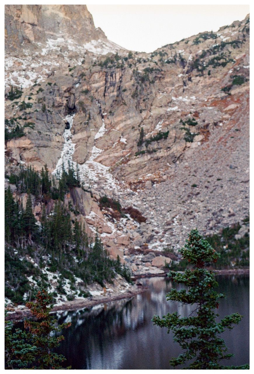 A rock face and snowmelt waterfall above a dark alpine lake